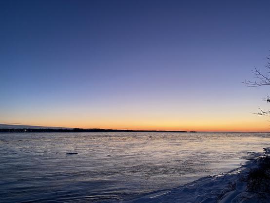 The St. Lawrence River at dusk. The water is flowing. The sky is in a dark blue to orange gradient from top to bottom.
- - -
Le fleuve Saint-Laurent au crépuscule. L'eau coule. Le ciel est dans un dégradé bleu foncé à orange de haut en bas.