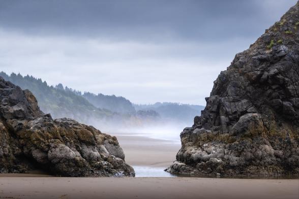 A soft, beautiful beach landscape with sea stacks and water in between them.