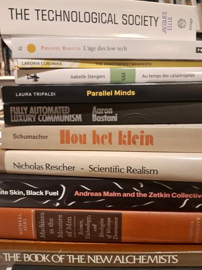 A pile of books, including "The Technological Society" by Jacques Ellul, "L'age des low tech" by Philippe Bihouix, "The Xenofeminist Manifesto" by Laboria Cuboniks, "Au temps des catastrophes by Isabelle Stengers, "Parallel Minds" by Laura Tripaldi, "Fully Automated Luxury Communism" by Aaron Bastani, "Hou het klein" by E.F. Schumacher, "Scientific Realism" by Nicholas Rescher, "White Skin, Black Fuel" by Andreas Malm and the Zetkin Collective, "Machines as the Measure of Men" by Michael Adas and "The Book of the New Alchemists".