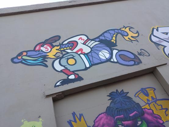 All these pictures are super colored graffiti in the facade of the same building. This one looks like a anthropomorphic animal with a long moustache, playing rugby or American football.