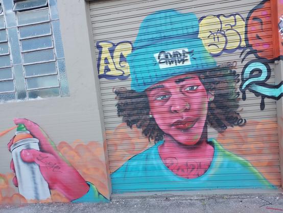 All these pictures are super colored graffiti in the facade of the same building. This one is a purple teenager holding a can of spray paint.