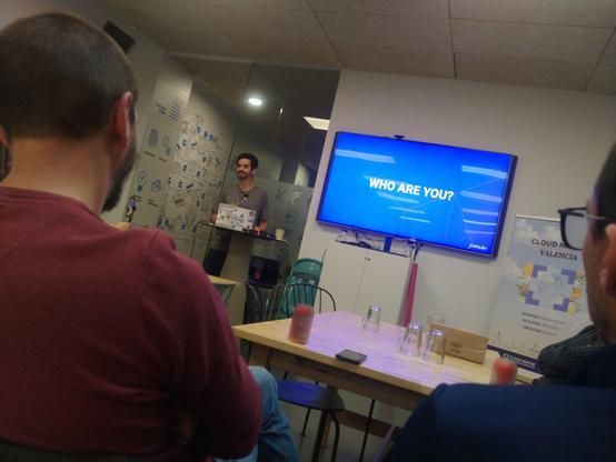Juliano Costa presenting in a tv meeting room during the CLOUDNATIVEVALENCIA CNCF event at FLYWIRE