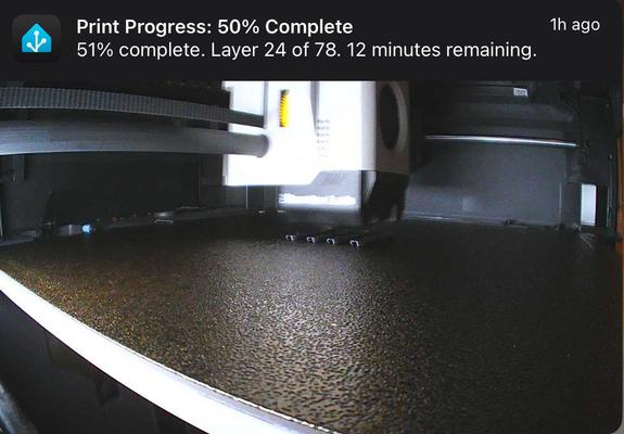 A push notification from Home Assistant. Includes a photo of the inside of a 3D printer. Title reads: “Print Progress: 50% Complete”. Text reads: “51% complete. Layer 24 of 78. 12 minutes remaining.”