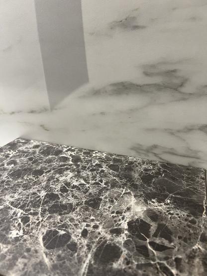 A close-up of two types of marble surfaces: a dark, speckled black marble with white veining at the bottom and a lighter, smooth marble with subtle gray patterns above it. The image captures texture and contrast between the materials.