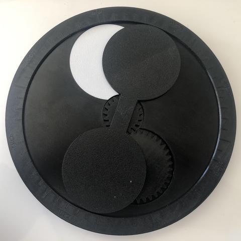 Physical moon phase calculator, made out of 3d printed parts and gears. The device is black and round, with a white calendar pointer on one side and a moveable moon phase indicator on the other.