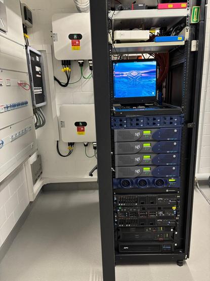 photo of the server rack with four Origin300 servers running connected to numalink router. in the background, two solar inverters on the wall.