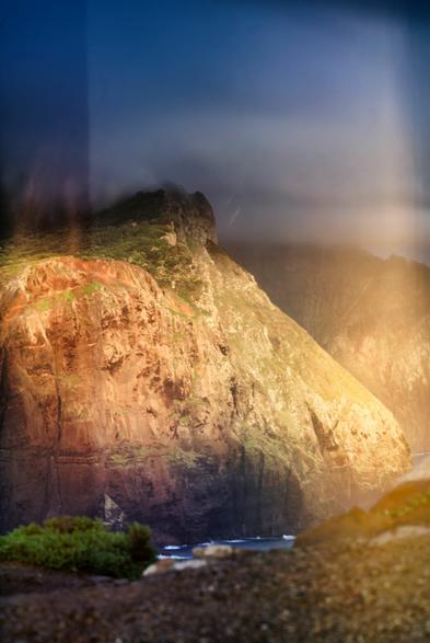 Ein von der Sonne angestrahlter Felsen vor dunklen Hintergrund. An den Rändern des Bildes sind die Effekte des nicht abgedeckten Sucher zu sehen.