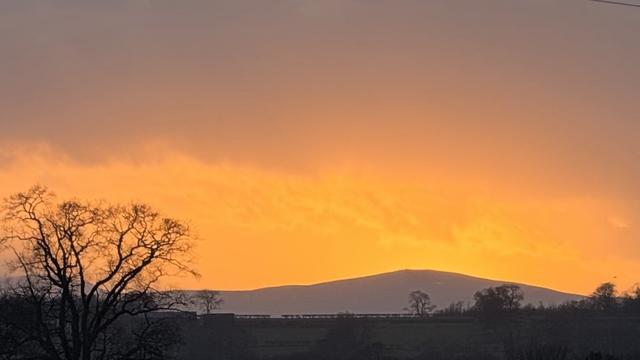 Stormy sky, mountain in silhouette with some winter trees, a vivid golden orange sunset