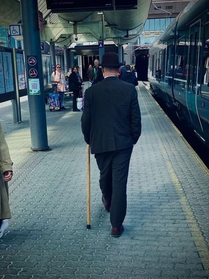 Dapper gentleman in #tophat, suit and a cane walking on the train station. Photo taken from behind. Oslo Centralstation