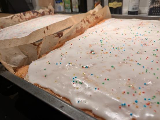 close up of a cake still in the pan with white frosting and colorful sprinkles