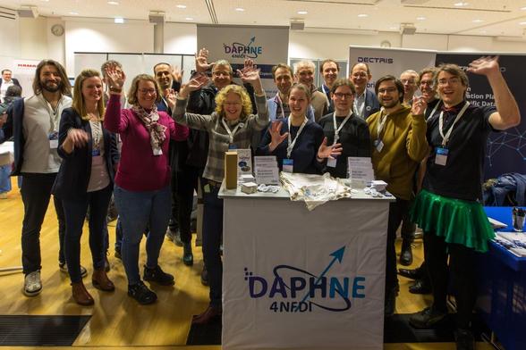 Gruppenbild fröhlich des fröhlich winkenden Daphne-Teams an ihrem Stand bei einer Postersitzung.
