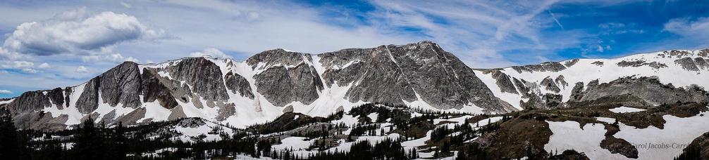Medicine Bow Peak, a massive grey mountain, its flanks riddled with snow fields, is a challenging climb any time of year.  Here, in summer, it looms against a blue sky with incoming storm clouds.
I often take scenic highways to avoid the interstates.  This area has fond memories for me.  I did my master's work up in the Snowy Range, and have fond memories of snowstorms in July, trying to collect samples in the driving rain (plus lightning! thunder! above the treeline!)  in August thunderstorms, and wearing orange vests so that the hunters wouldn't shoot me in fall.