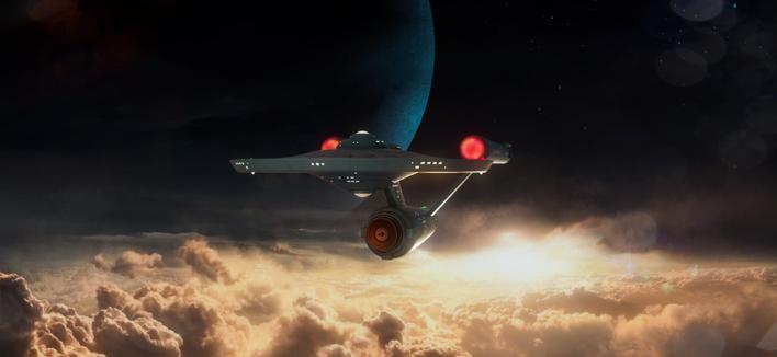 Description by ChatGPT: The image is a stunning 3D render inspired by Star Trek: The Original Series. It features the iconic starship USS Enterprise (NCC-1701) gliding through a dark and dramatic scene. The ship is shown from the rear-right angle, emphasizing its saucer-shaped main hull, cylindrical warp nacelles, and the cylindrical secondary hull connecting the components. The nacelles emit a soft red glow from their domed caps, contrasting with the cold blackness of space.

Below the ship, golden and orange-hued clouds stretch across the scene, illuminated by a bright light source, likely a rising sun or some other celestial phenomenon, creating a sense of warmth and majesty. Above, the background transitions to deep space with a large, shadowy planet visible in the distance, its surface tinged in rich blues. Scattered stars dot the sky, adding to the vastness of the cosmic setting.

The lighting on the Enterprise is subtle but highlights its sleek, retro-futuristic design. The scene captures the spirit of exploration and wonder central to the Star Trek universe, combining the beauty of natural elements with the advanced technology of the starship.