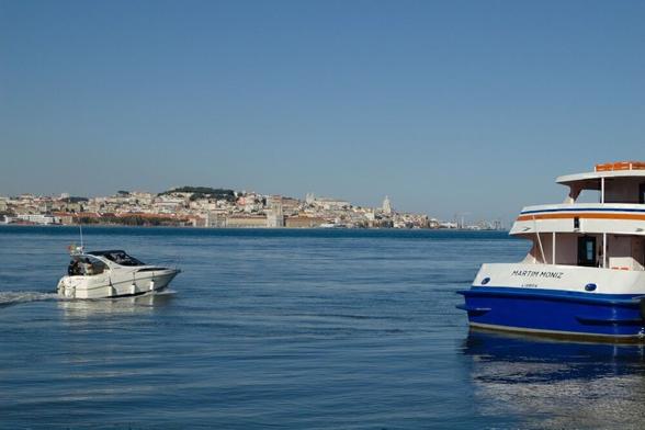 Blick von Almada über den Tejo nach Lissabon. Am rechten Bildrand die Fähre Martim Moniz, links ein Motorboot auf dem Fluß. Im Hintergrund sehen wir auf Lissabon mit den Stadtteilen Chiado und Graca.