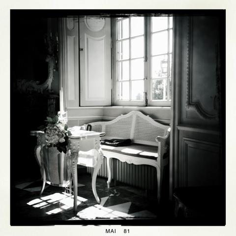 Black and white photo, taken with Hipstamatic, shows a large window in a castle through which light falls into the room. The bride's bouquet lies on a table in front of the window.