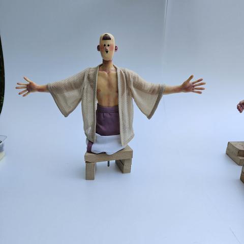 A stopmotion puppet with a very cartoony face is wearing a kimono jacket made with a very light fabric. We can see the puppet body through trabsparency.