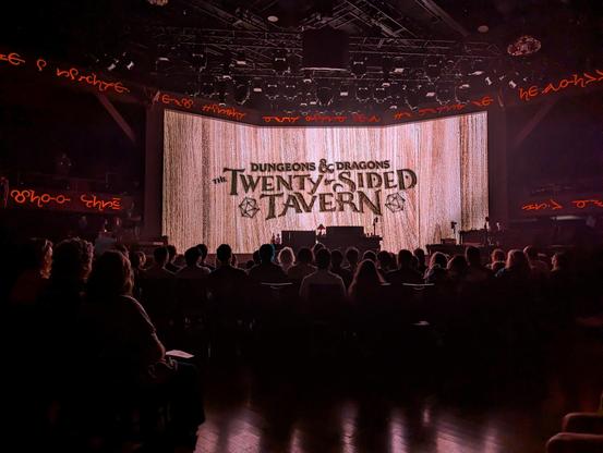 View from the seat towards the stage, where the show title is projected on a wide screen. The venue is darkened.