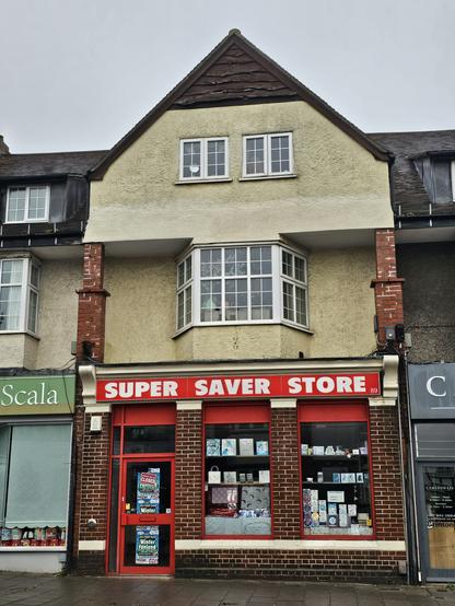 Photograph of a shop front, with cards and decorative paper bags in the windoe. The shop sign above the window reads 'SUPER SAVER STORE' in ALLCAPS san serif.
