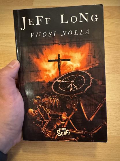 Kuvassa pitelen kädessä kirjaa. Kirja on Vuosi Nolla, jonka on kirjoittanut Jeff Long. Kannessa on luurankoja, ristiinnaulitsemista ja tulta, eli vähän kaikenlaista mikä antaa osaltaan osviittaa kirjan sisällöstä mutta ei mielestäni ihan täysin kuitenkaan.