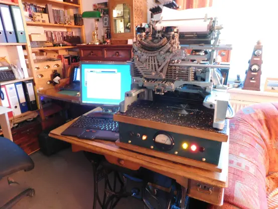 Zu sehen ist ein Büro mit einem Fernschreibempfänger der Firma Lorenz im Vordergrund.
Unter dem Fernschreiber befindet sich der Steuerungscomputer.