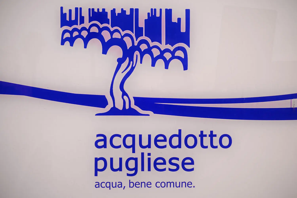 Wegmarkierung / Logo des 
acquedotto Pugliese
acqua, bene comune.

Über dem Text stilisiert ein Olivenbaum an einem Bach, darüber dem eine grobe Stadt-Siluette