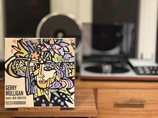 Gerry Mulligan Meets Ben Webster LP cover.

A sort of modernist drawing of a woman wearing a flower-covered hat.

The black LP plays on a vintage, restored Bang & Olufsen Beogram 8002 linear-tracking turntable to the right.