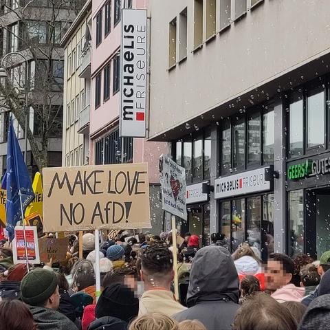 Foto des Demozugs von hinten. Ein Plakat mit "Make Love No AfD!", eine blaue Flagge und große gelbe Sterne werden aus der Menge hochgehalten. Über der Menge fliegen viele kleine Seifenblasen.