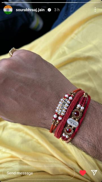 Four deep-red rakhi wrist bands with gleaming gold, white, pearl, ruby and silver beads are tied around a seated man's wrist, seen from above, over a lustrous yellow kurta with blue denim jeans and trainers, out of focus, below. The photograph was posted as an Instagram story by Sourabh Raaj Jain around midday on Aug. 31, 2023.