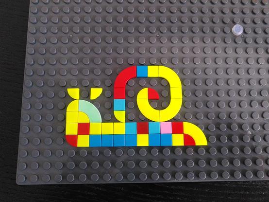 Lego bricks on a baseplate, they form the silhouette of a snail.