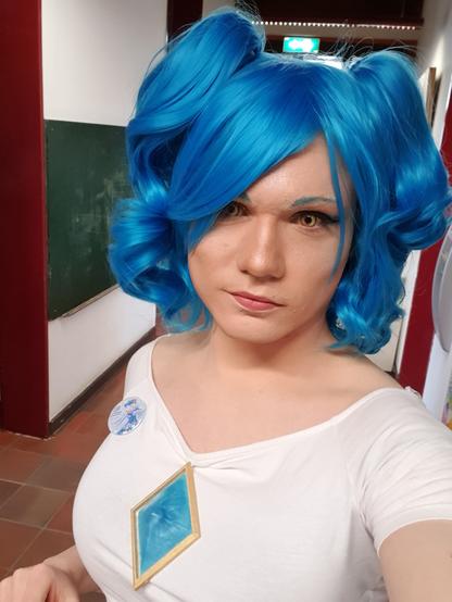Cosplay of a blue haired girl character with a large blue crystal on her chest.