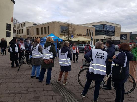 eine Gruppe Menschen. Viele mit Besten der Omas gegen Rechts . Im Hintergrund ein Blaues Zelt