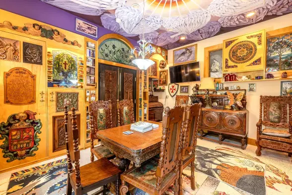 Spot! That! Templar cross! 

Any visual respite which may have been offered by this room's cream walls is immediately negated by the fact that all the walls are covered with pseudo-medieval and/or religious carvings, and that the ceiling is painted with a purple mural of folded angels' wings. The furniture is all ornately carved, pseudo-late medieval and looks deeply uncomfortable to sit at or use.
