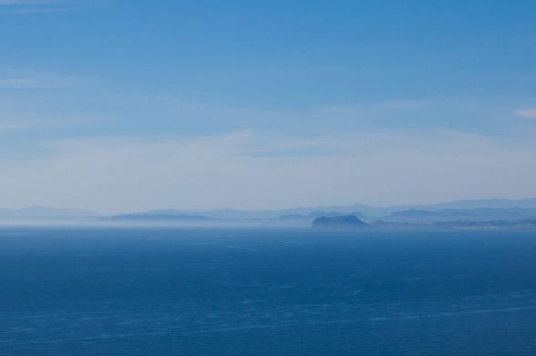 A blue sky with several clouds and the see. In the middle there is a haz covering several mountains in the shore. Taken in Cabo Tiñoso (Cartagena)