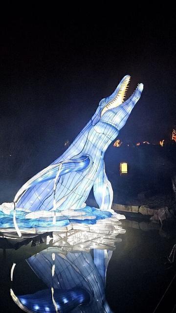 A giant water dinosaur throws itself up into the air out of a pond, like wales often do. It looks like a giant crocodile, maw wide open, but with fins. It glows in light blue, which gets reflected in the dark water. It's at least 7 or 8 meters high.