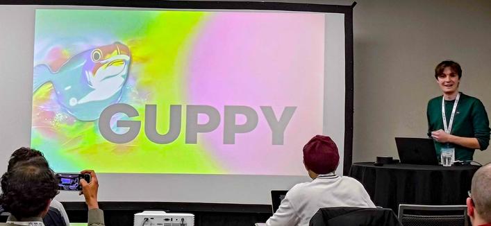 Mark Koch standing next to a psychedelic image of a fish.  The text says "GUPPY".