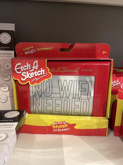 An etch a sketch in a box on a store shelf. On the screen in large letters is printed “no wifi needed”.
