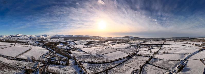 panorama over snowy fields and village, with cloud streaked skies and in far distance lake and mountains