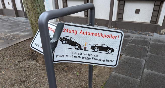 Ein verbeultes und halb abgerissenes Blechschild mit dem Hinweis "Achtung Automatikpolleranlage"