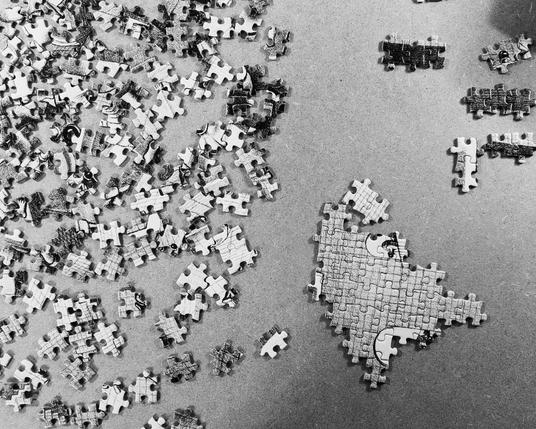 Black & white photo of a grey scale puzzle, some sections attached, left half side all loose pieces.