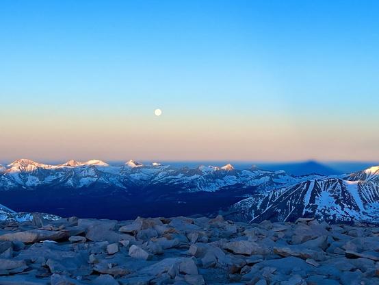 the full moon setting viewed from on top of a mountain at sunrise