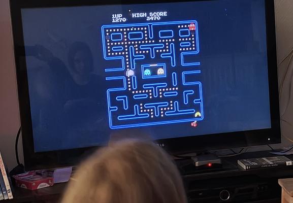 a big lcd screen showing a pacman game.. kid sitting in front, chasing dad's high score :)