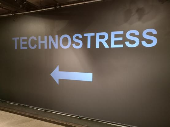 Bühnenbild: Wort "Technostress" und ein Pfeil nach links.