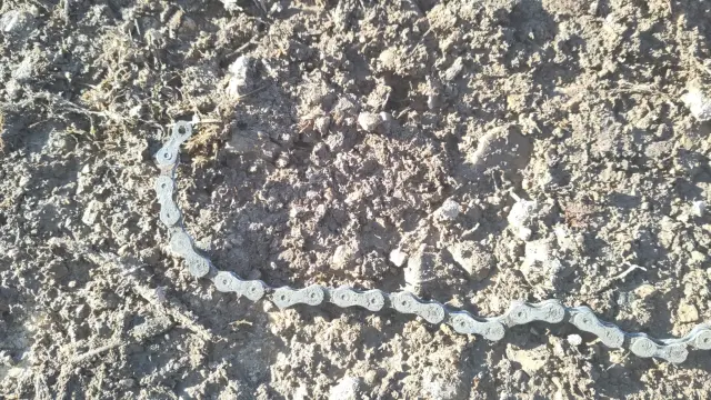 Eine gerissene Fahrradkette liegt auf einem matschigen Waldweg