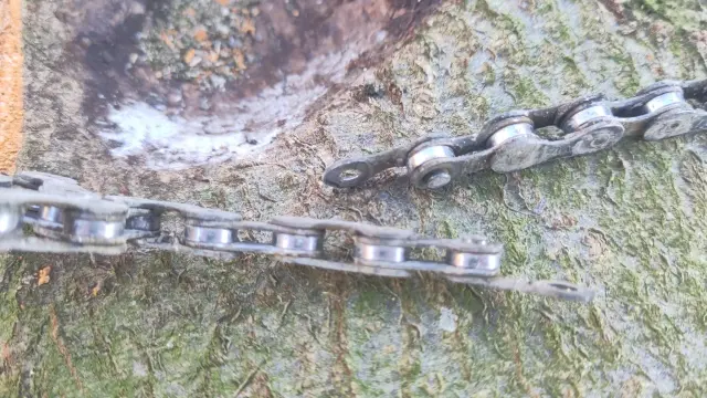 Eine gerissene Fahrradkette liegt auf einem Baumstamm. In der Mitte sieht man die gerissene Lasche.