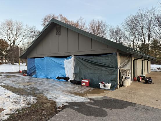 A city park building with tarps hung around one end to create a semi-enclosed shelter.