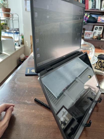 A laptop open at an angle on a Lego stand. The screen displays a landscape background. A 2nd screen below and covering the keyboard is reflecting light. A hand is visible to the left