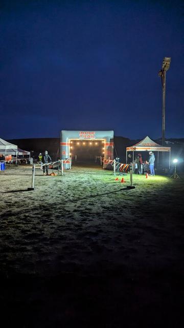 Well lit arch over the start/finish line at night. Other canopies nearby.
