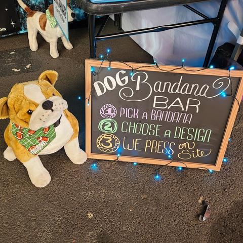 Our Dog Bandana Bar sign lit up with blue lights and our demo dog a tan and white Bulldog wearing our small foodball Bandana that says "TOUCHDOWN!"