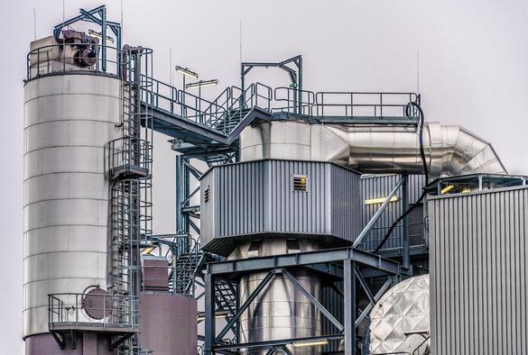 The image shows an industrial structure, possibly part of a factory or processing plant. It features large metal silos, pipes, and various metal frameworks often used in such facilities. The equipment and design are typical of places involved in manufacturing, processing, or power generation.