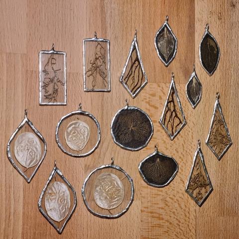 Some handmade stained glass pendants. Between the glass planes are lunaria discs, plants roots, skeleton leaves and hydrangea petals. The latter have a black background so they stand out more on the skin.